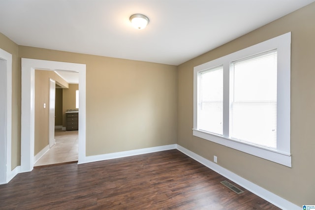 spare room featuring dark wood-style flooring, visible vents, and baseboards