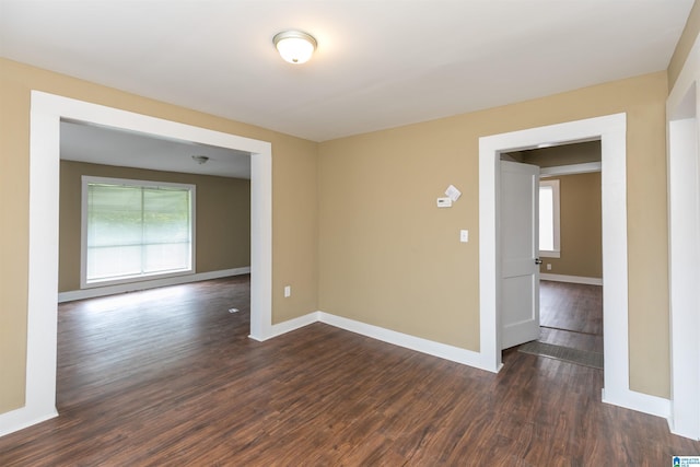 empty room with dark wood-style floors, a healthy amount of sunlight, and baseboards