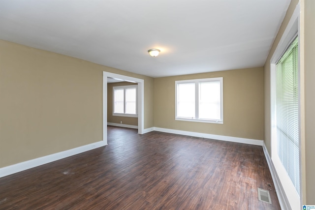 unfurnished room with baseboards, visible vents, and dark wood-style flooring