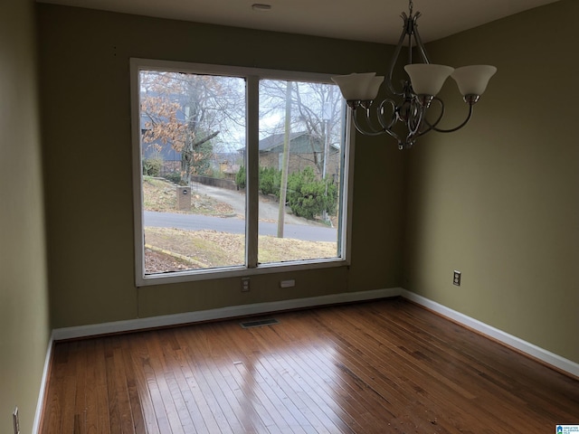 unfurnished dining area with dark wood-style floors, baseboards, visible vents, and a chandelier