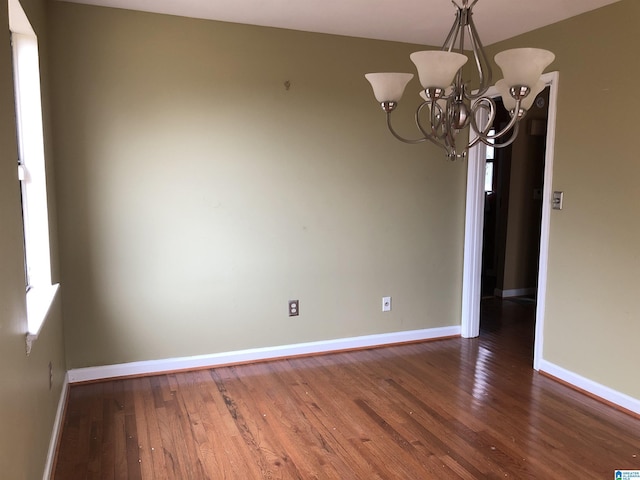 empty room featuring an inviting chandelier, baseboards, and hardwood / wood-style floors