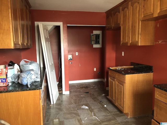 kitchen with dark stone counters, brown cabinetry, electric panel, and baseboards