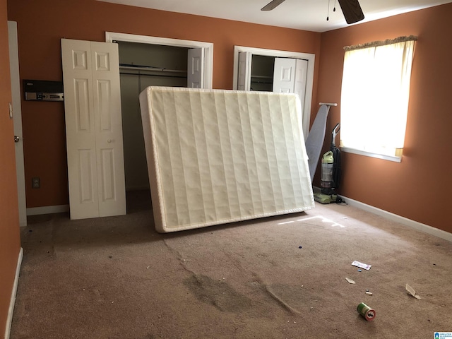 unfurnished bedroom featuring ceiling fan, carpet floors, two closets, and baseboards