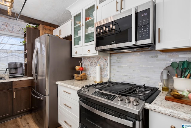 kitchen featuring decorative backsplash, glass insert cabinets, appliances with stainless steel finishes, a textured ceiling, and white cabinetry