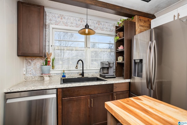 kitchen with pendant lighting, appliances with stainless steel finishes, a sink, dark brown cabinetry, and butcher block countertops