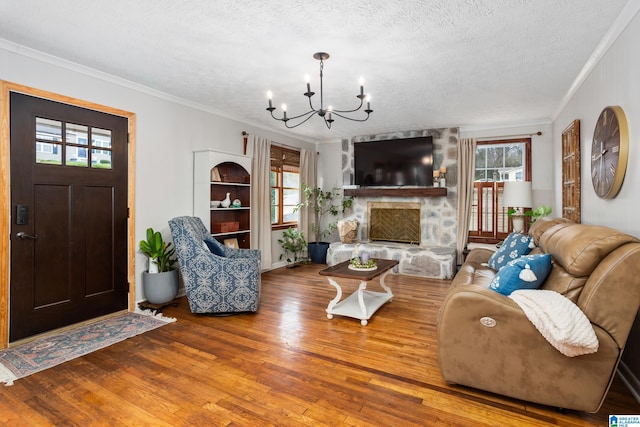 living area featuring a fireplace, an inviting chandelier, ornamental molding, a textured ceiling, and wood finished floors