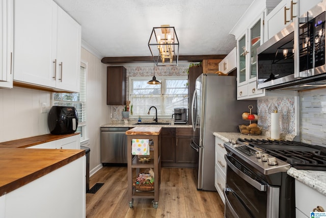 kitchen featuring light wood finished floors, stainless steel appliances, glass insert cabinets, a sink, and wood counters