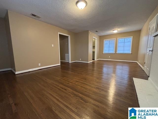 spare room with visible vents, a textured ceiling, baseboards, and wood finished floors