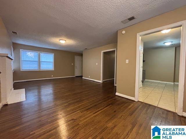 unfurnished living room featuring a textured ceiling, a fireplace, wood finished floors, and visible vents