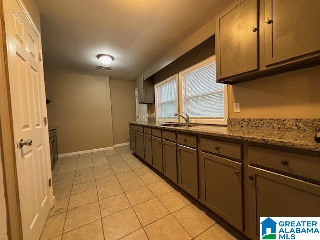 kitchen featuring light tile patterned floors, baseboards, gray cabinets, stone counters, and a sink