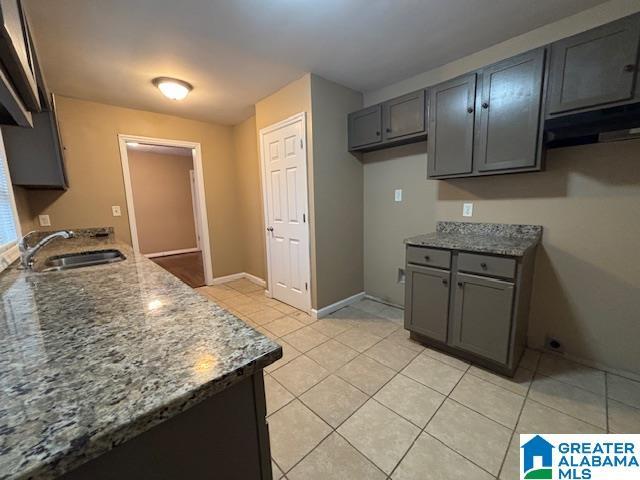 kitchen featuring stone counters, gray cabinets, light tile patterned flooring, and a sink