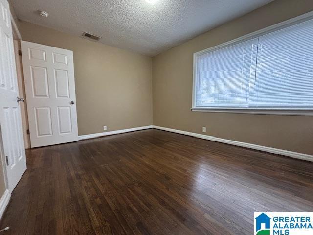 empty room with visible vents, a textured ceiling, baseboards, and wood finished floors