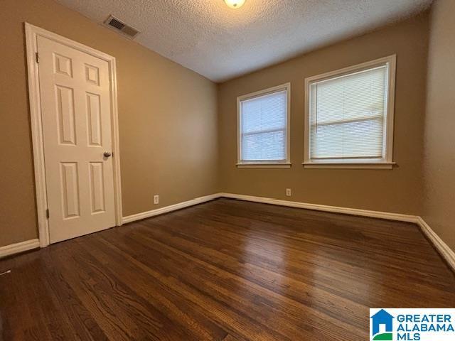 unfurnished room featuring a textured ceiling, dark wood-style flooring, visible vents, and baseboards