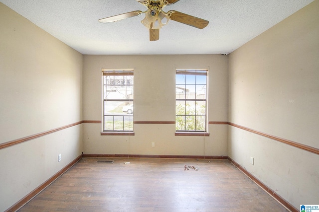 unfurnished room with a wealth of natural light, a textured ceiling, visible vents, and wood finished floors