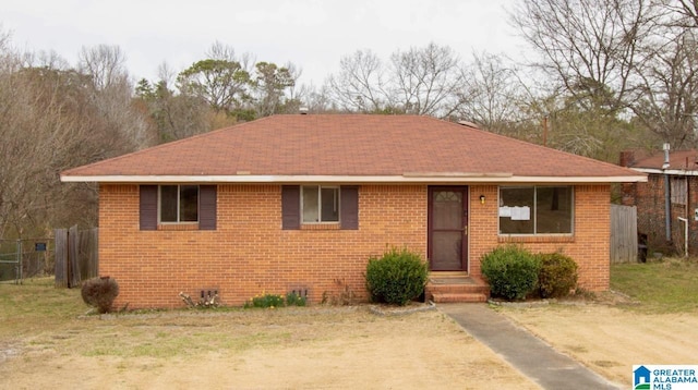 view of front of property featuring brick siding, roof with shingles, and fence