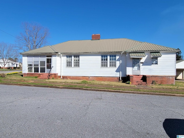 view of front of home with entry steps, metal roof, and a chimney