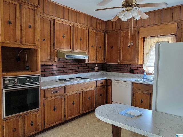 kitchen featuring under cabinet range hood, white appliances, a sink, light countertops, and brown cabinets