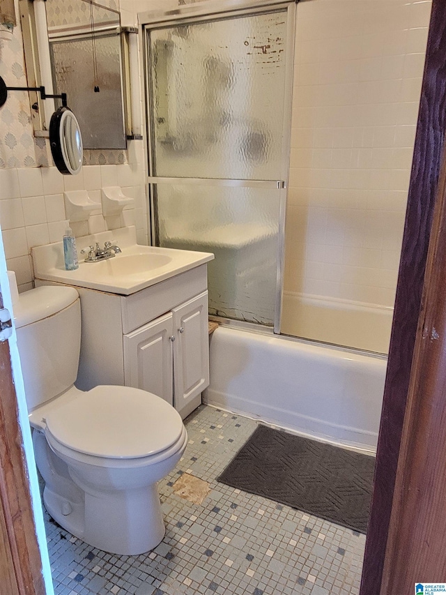 bathroom featuring tile walls, bath / shower combo with glass door, toilet, vanity, and tile patterned floors