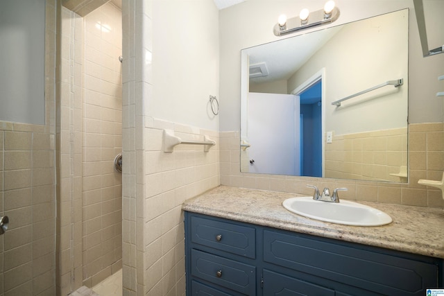 full bathroom with a wainscoted wall, vanity, tile walls, and tiled shower