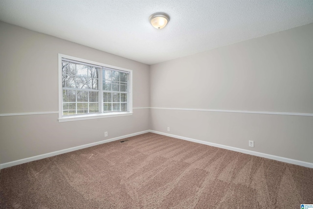 spare room with a textured ceiling, carpet floors, and baseboards