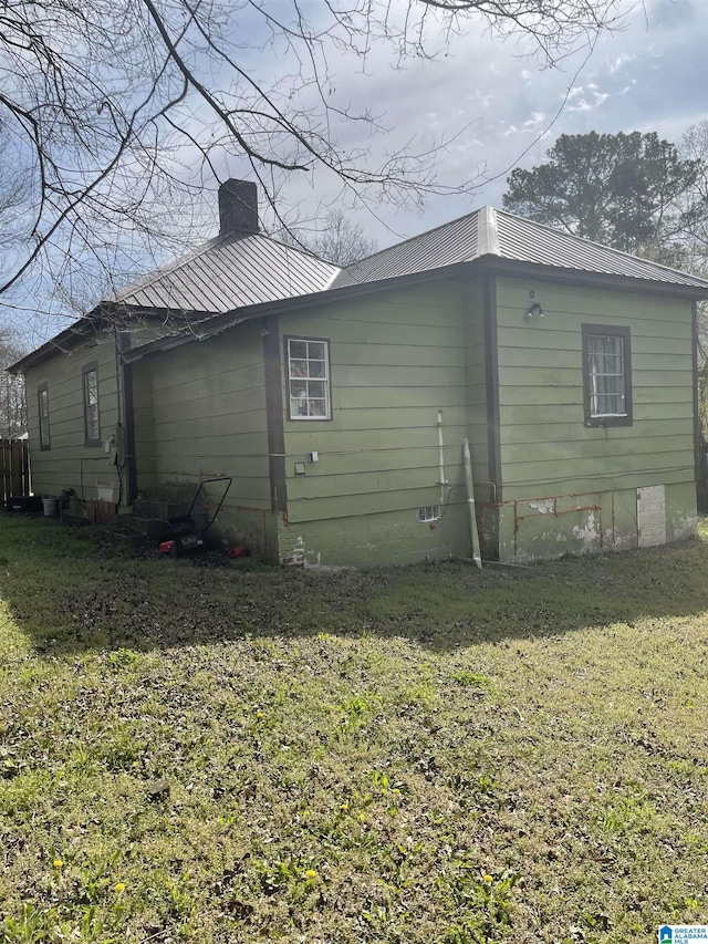 view of side of property with crawl space, a chimney, metal roof, and a yard