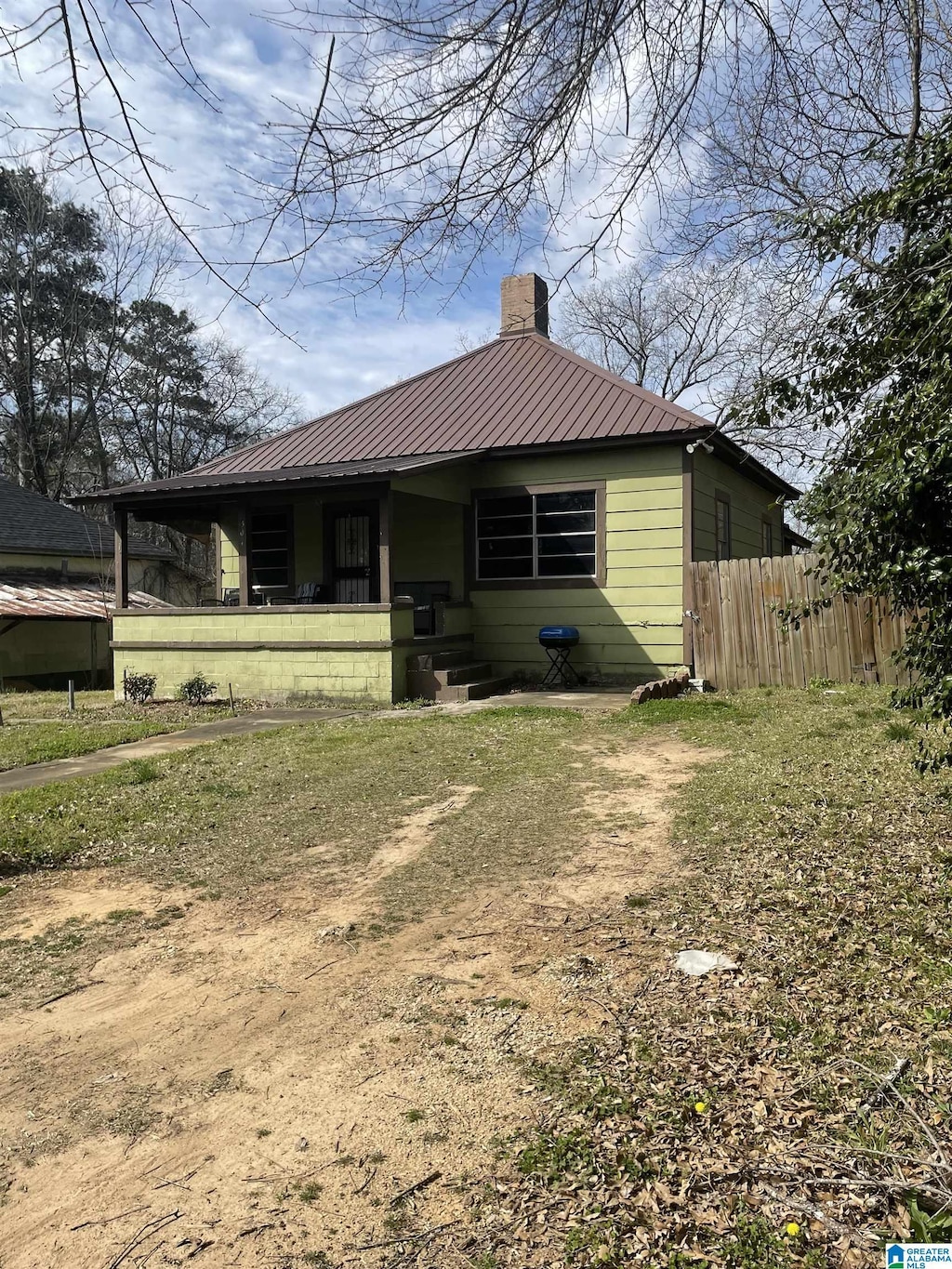 bungalow-style house with dirt driveway, a chimney, fence, and metal roof