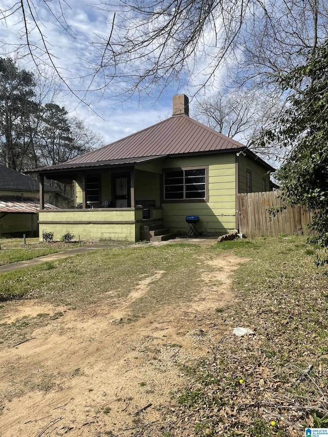 bungalow-style house with dirt driveway, a chimney, fence, and metal roof