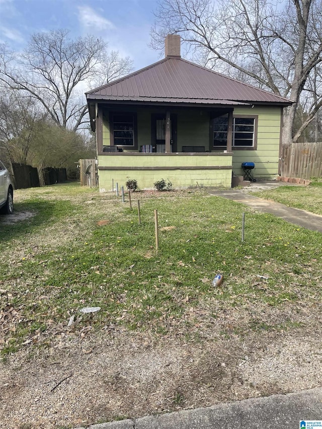 bungalow-style home with a chimney, fence, metal roof, and a front yard