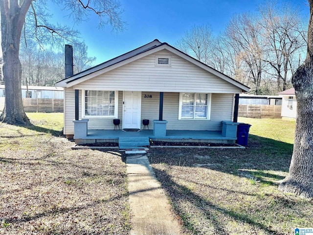 bungalow-style home with covered porch, fence, a chimney, and a front lawn