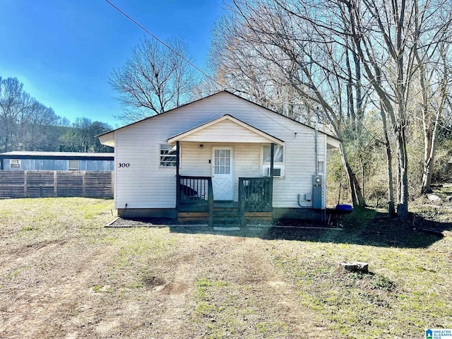 bungalow featuring covered porch, fence, and a front lawn