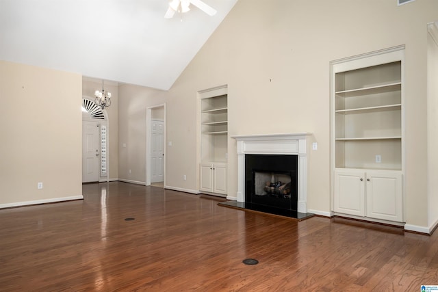 unfurnished living room with a fireplace with raised hearth, built in shelves, ceiling fan with notable chandelier, wood finished floors, and baseboards