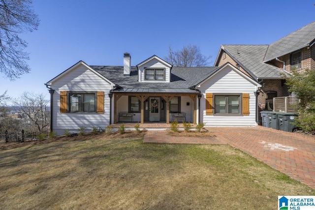 view of front of property featuring covered porch, a chimney, and a front lawn