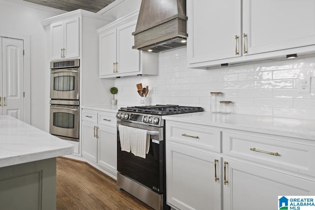 kitchen featuring dark wood finished floors, stainless steel appliances, custom range hood, decorative backsplash, and white cabinetry