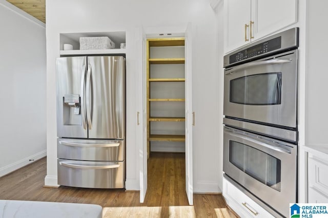 kitchen with baseboards, white cabinetry, stainless steel appliances, and wood finished floors