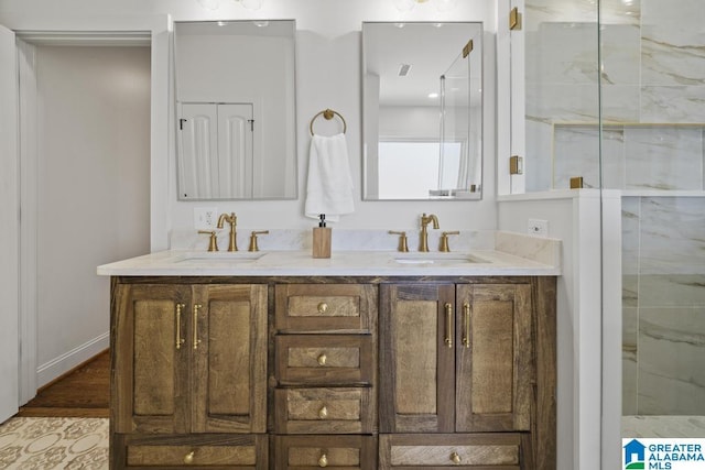 bathroom with double vanity, a marble finish shower, baseboards, and a sink