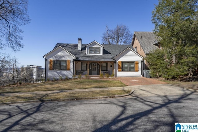 view of front of home with a front yard, covered porch, fence, and a chimney