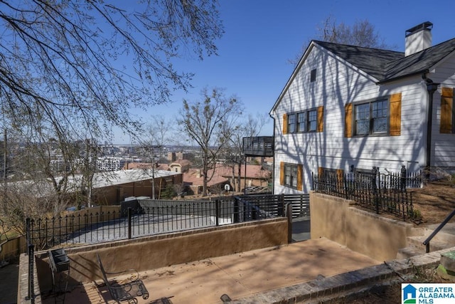 view of property exterior with a fenced front yard, a chimney, and a balcony