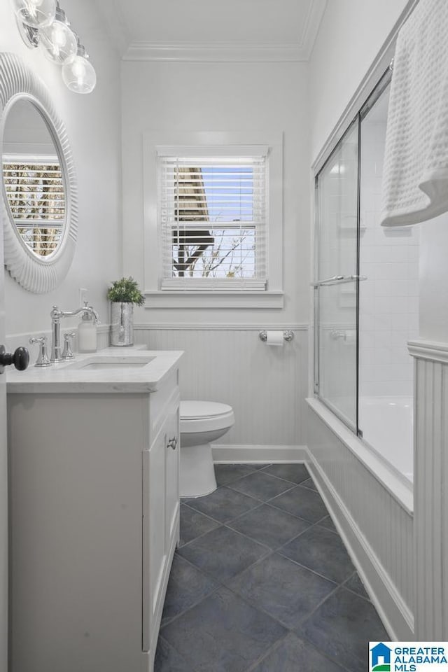 bathroom with toilet, a wainscoted wall, vanity, combined bath / shower with glass door, and crown molding