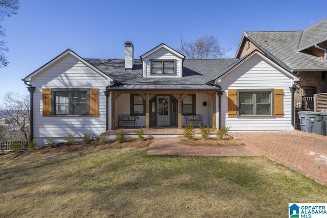 view of front facade with covered porch, a shingled roof, a chimney, and a front lawn