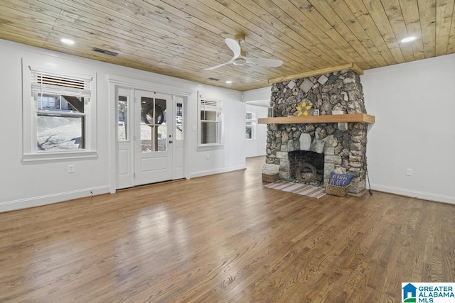 unfurnished living room with a ceiling fan, wooden ceiling, a stone fireplace, and wood finished floors