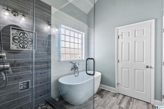 bathroom featuring a tile shower, a freestanding tub, and baseboards