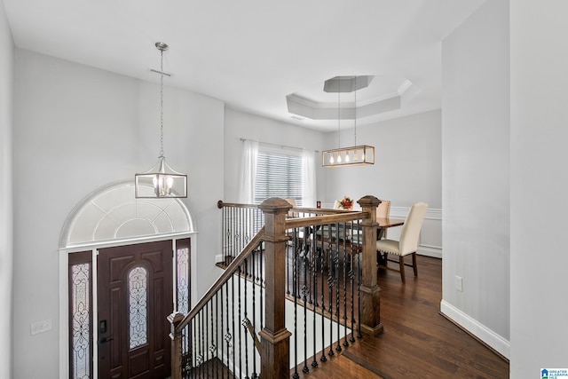 foyer featuring baseboards, wood finished floors, a tray ceiling, crown molding, and a notable chandelier