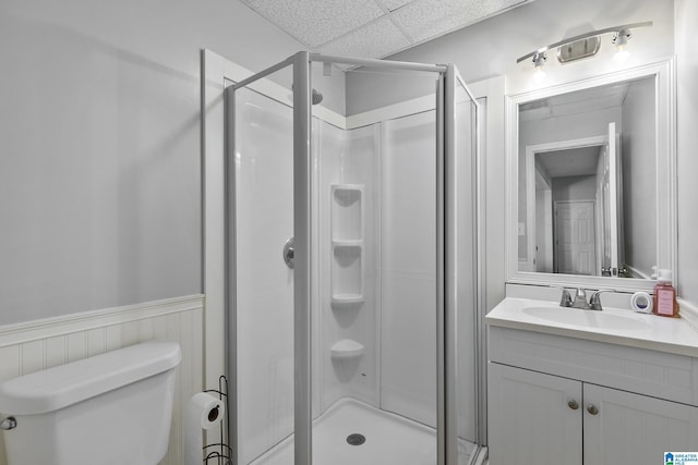 full bathroom with wainscoting, toilet, vanity, a paneled ceiling, and a shower stall