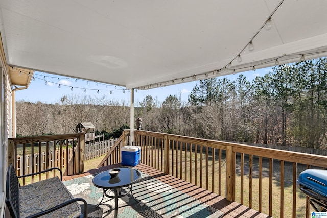 deck featuring a yard, outdoor dining space, fence, and a view of trees