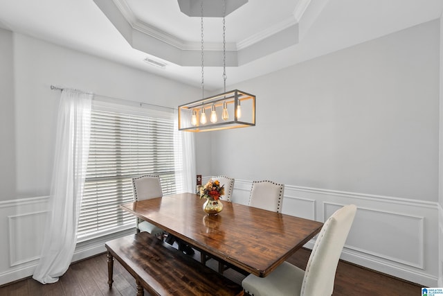 dining area with ornamental molding, a tray ceiling, a wainscoted wall, and dark wood finished floors