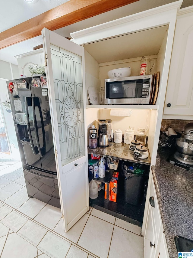 kitchen featuring light tile patterned floors, white cabinetry, backsplash, black refrigerator with ice dispenser, and stainless steel microwave