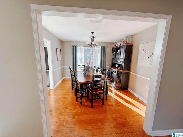 dining room with a notable chandelier, light wood-style flooring, visible vents, and baseboards