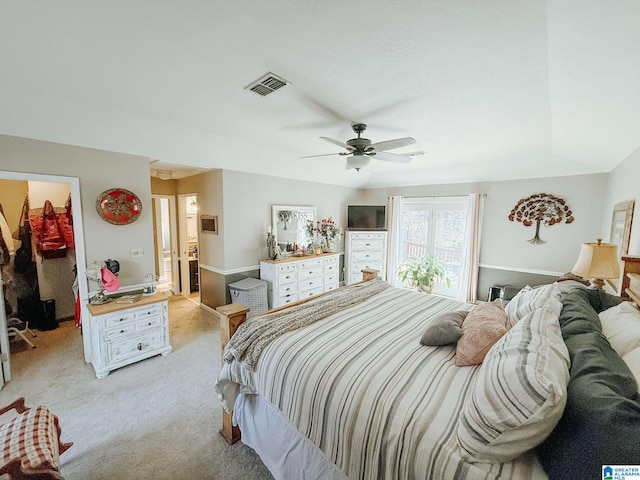 bedroom with ceiling fan, ensuite bathroom, light colored carpet, visible vents, and a walk in closet