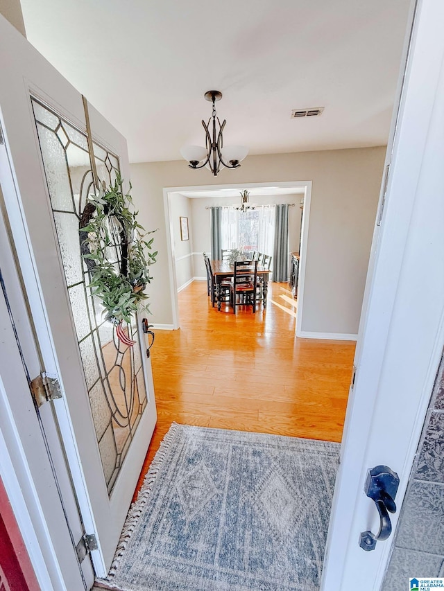 corridor featuring light wood finished floors, baseboards, visible vents, and a notable chandelier