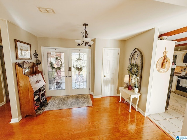 foyer with baseboards, visible vents, french doors, light wood-type flooring, and a chandelier